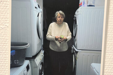 Eine Person steht zwischen Waschmaschinen und Trocknern und schaut in die Kamera.